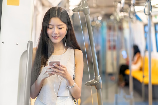 Passager d'une jeune femme asiatique écoutant de la musique via un téléphone mobile intelligent dans une rame de métro