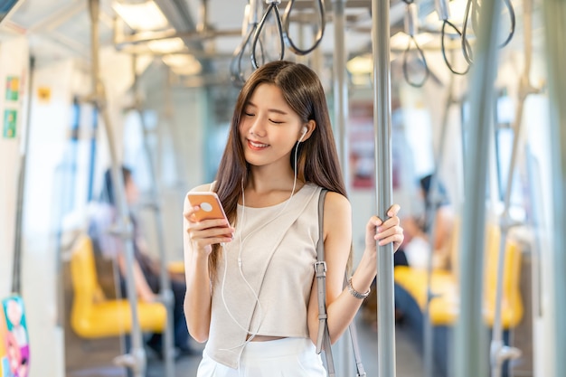 Passager d'une jeune femme asiatique écoutant de la musique via un téléphone mobile intelligent dans une rame de métro