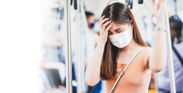 Passager d'une jeune femme asiatique portant un masque chirurgical et ayant mal à la tête dans une rame de métro