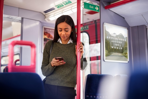 Passagère debout près des portes du train en regardant un téléphone mobile