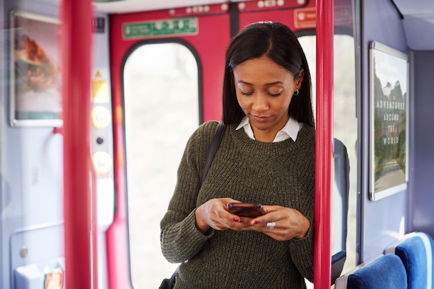 Passagère debout près des portes du train en regardant un téléphone mobile