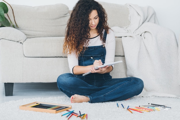 passe-temps artistique et loisirs. dame assise détendue jambes croisées sur le sol, dessinant avec des crayons de couleur.