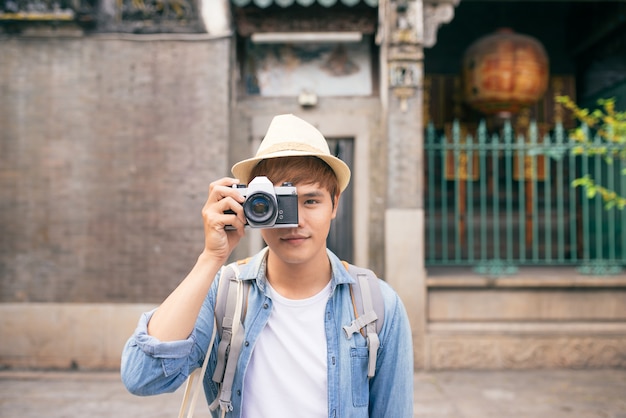 Passe-temps et voyages. Jeune homme avec sac à dos prenant une photo avec son appareil photo dans une rue asiatique.