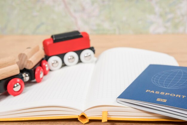 passeport biométrique et un petit train en bois sur un journal ouvert posé sur une table en bois contre une carte