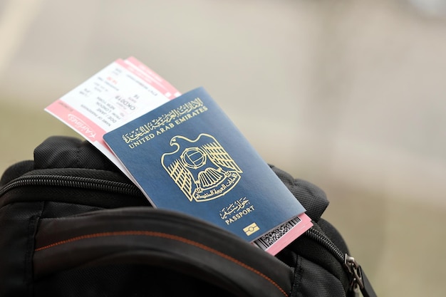 Photo passeport bleu des émirats arabes unis avec des billets d'avion sur un sac à dos touristique
