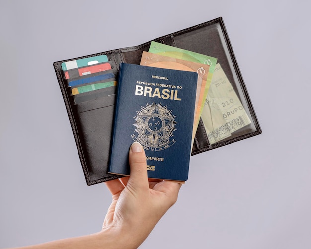 Passeport brésilien dans une main avec portefeuille cartes de crédit et billets en euros sur fond blanc