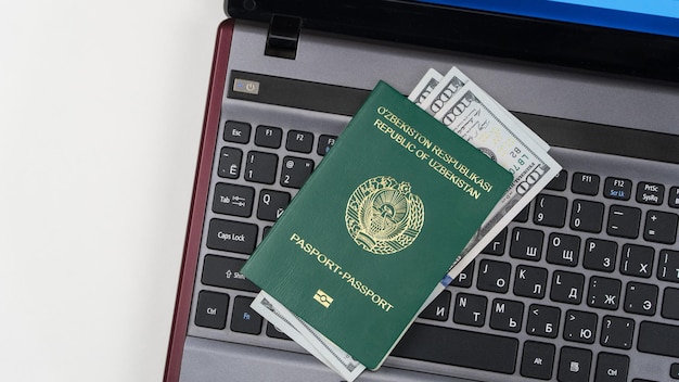 Passeport de l'Ouzbékistan avec des dollars américains sur le clavier de l'ordinateur portable Inscription en ligne