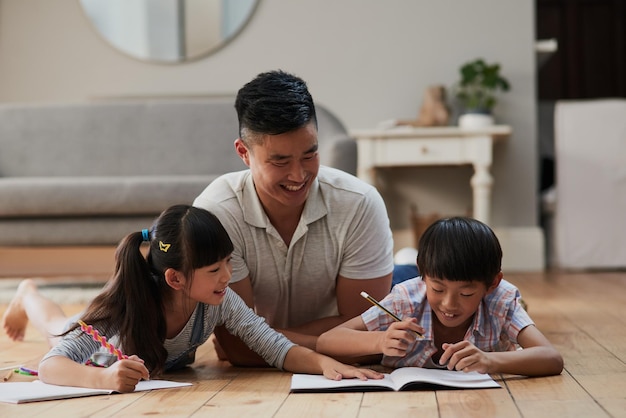 Passer du temps avec mes enfants Photo d'un père joyeux et de ses deux enfants faisant leurs devoirs ensemble allongés sur le sol à la maison pendant la journée