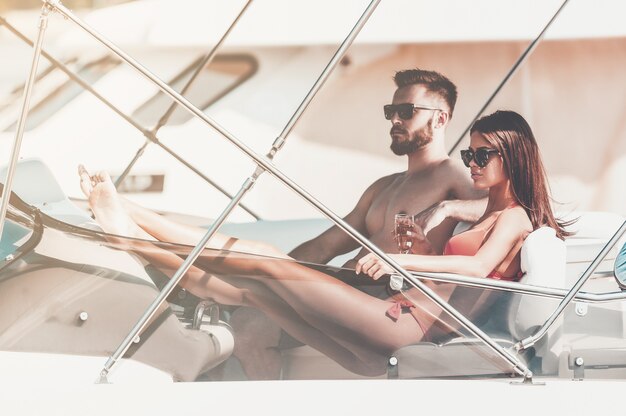 Passer du temps sans soucis sur un yacht. Beau jeune couple impatient alors qu'il était assis sur le bord du yacht