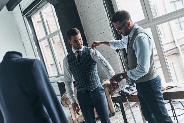 passer en revue les détails. jeune designer à la mode mesurant la manche des clients