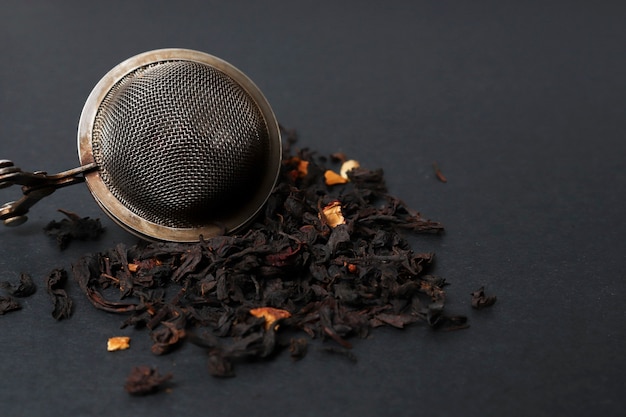 Une passoire à thé et une lame de thé naturel sec pour préparer une boisson réchauffante sur fond sombre