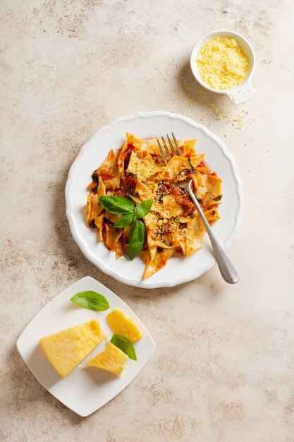 Pasta Maltagliati avec sauce tomate classique, parmesan et basilic sur un fond de table lumineuse en béton rustique. Plat traditionnel italien au service. Vue de dessus.