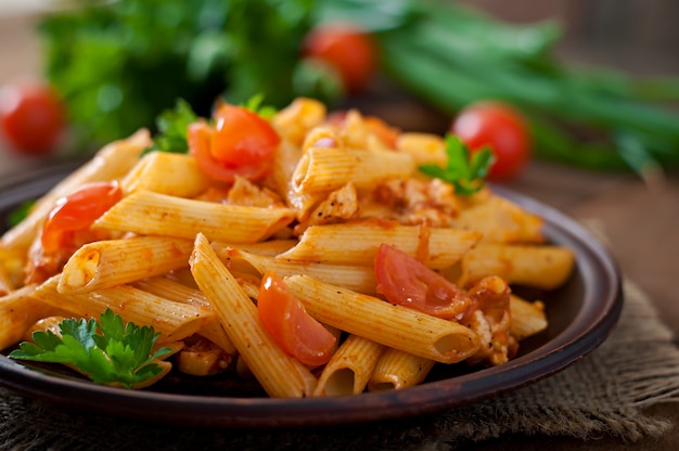 Pasta Penne dans de la sauce tomate avec du poulet et des tomates sur une table en bois