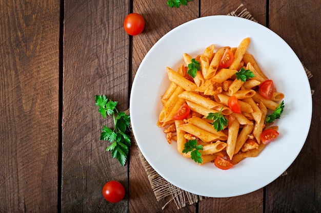 Pasta Penne dans de la sauce tomate avec du poulet et des tomates sur une table en bois