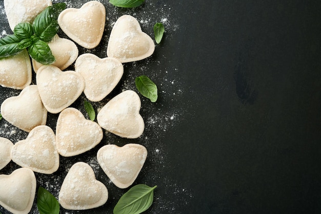 Pasta de ravioli italien en forme de cœur Ravioli cru et savoureux avec de la farine et du basilic sur fond sombre Ingrédients de cuisine Arrière-plan Idées de déjeuner pour la Saint-Valentin ou la fête des mères Vue supérieure avec espace de copie