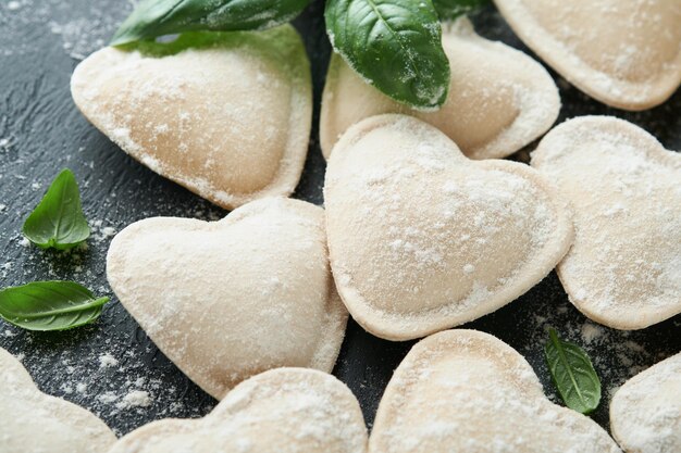 Pasta ravioli italien en forme de cœur Ravioli crus savoureux avec de la farine et du basilic sur un fond sombre Ingrédients de cuisine de fond Idées de déjeuner pour la Saint-Valentin ou la fête des mères Vue supérieure avec espace de copie