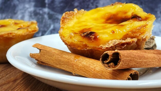 Photo un pastel de nata ou tarte aux œufs portugaise et des bâtons de cannelle sur une assiette blanche pastel de belm est une petite tarte avec une croûte de pâtisserie croustillante et une farce de crème à la crème