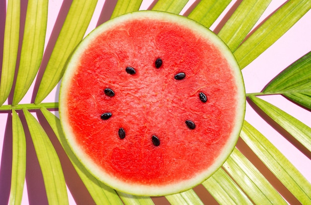 Pastèque sur des feuilles de palmier tropicales sur une surface rose