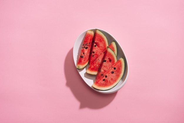 Pastèque en tranches fraîches dans un plat blanc sur une table rose.