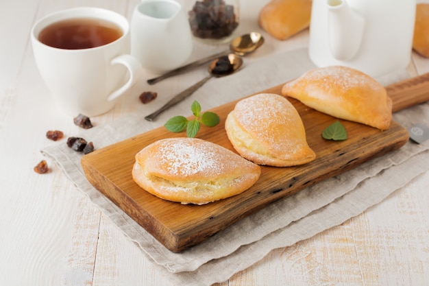 Pasties avec du fromage cottage et du sucre en poudre sur un fond en bois clair Pâtisserie traditionnelle russe Sochnik