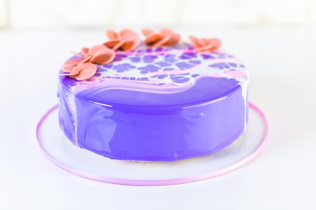 Pastre shef faisant un gâteau mousse avec glaçage miroir violet et décoré de fleurs rose chocolat.