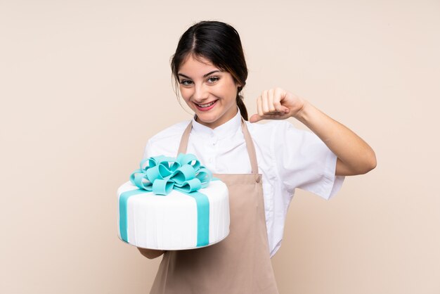 Pastry chef woman holding a big cake over wall isolated fier et satisfait de lui-même