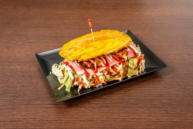 Patacon farci de tout le jambon laitue mijoté viande de poulet effiloché fromage frais plantain et ketchup avec mayonnaise sur une plaque noire