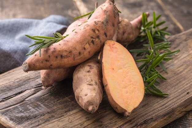 Patate douce sur fond de planche de bois, gros plan. Patates douces crues ou batatas aux herbes