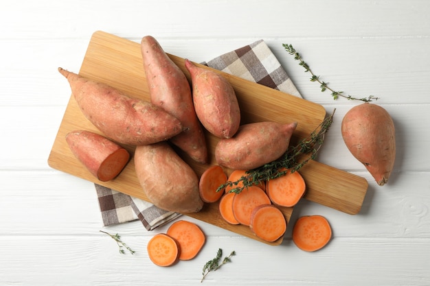 Patates douces, planche et serviette sur une surface en bois blanche