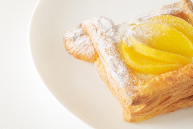 Pâte feuilletée sucrée avec crème de pêches et sucre en poudre sur plaque blanche vue de dessus mise au point sélective