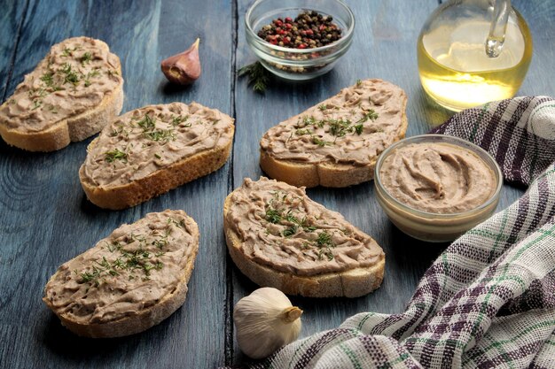 Pâté de foie de poulet frais fait maison avec des herbes sur du pain sur une table en bois bleue. Un sandwich.