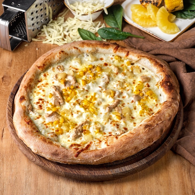 Pâte fraîchement cuite au jambon pizza hawaïenne et ananas sur une planche en bois entourée d'ingrédients individuels.