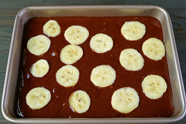 Pâte à gâteau au chocolat avec banane mûre coupée dans un moule à gâteau prêt à cuire