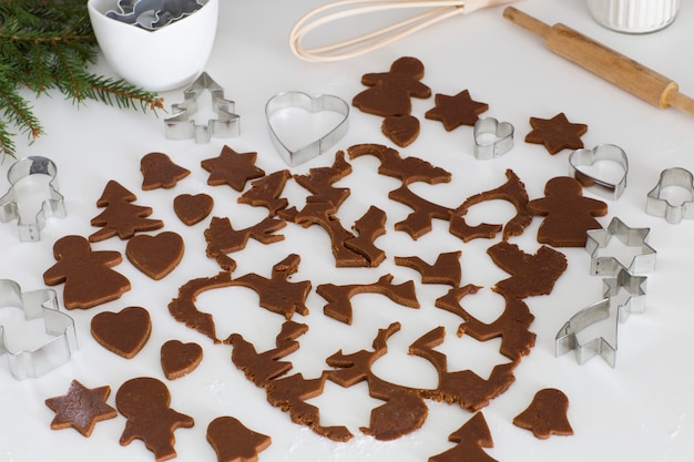 pâte de gingembre roulée, morceaux de pâte coupés pour biscuits, moules à pâtisserie, rouleau à pâtisserie, branches d'épinette