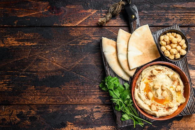 Pâte de houmous avec pain pita, pois chiches et persil dans un bol en bois. Fond en bois sombre. Vue de dessus. Espace de copie.