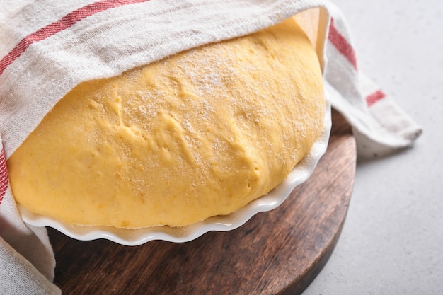 Pâte à levure crue à la citrouille dans un bol blanc recouvert d'une serviette sur la table de cuisine farinée, idée de recette. Concept maison faisant du pain, des petits pains ou du cinnabon ou faire de la pâte.