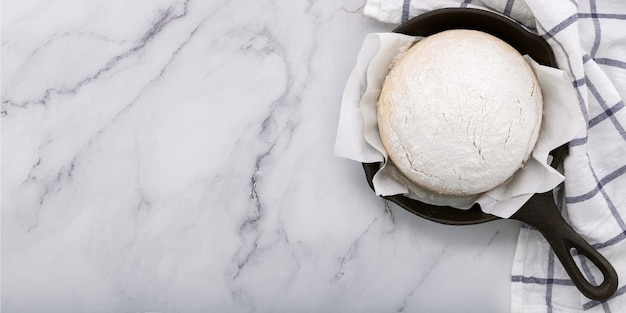 Pâte de levure maison crue fraîche reposant dans une poêle en fonte sur une table en marbre à plat.