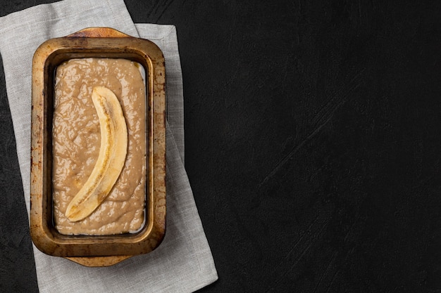 Pâte à pain aux bananes crues dans un plat de cuisson rectangulaire sur fond noir