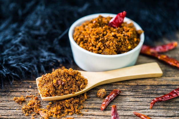 Photo pâte de piment de poisson séché épicé avec cuillère en bois et mur