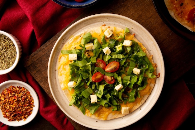 Pâte à pizza à l'arugula avec fromage et tomates cerise à l'intérieur d'une assiette en céramique faite à la main au-dessus d'une table en bois en vue de remorquage