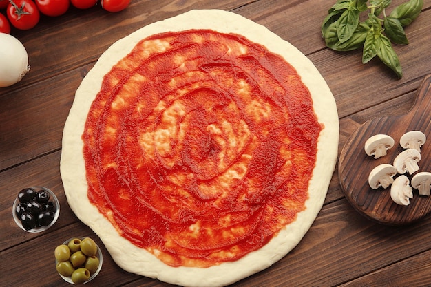 Pâte à pizza crue avec sauce et ingrédients sur table en bois