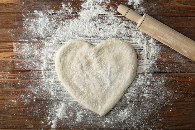 Pâte à pizza en forme de coeur avec de la farine sur la table