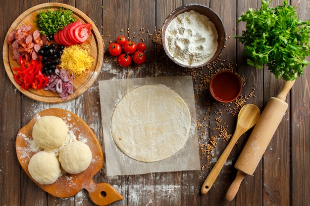 Pâte à pizza avec des ingrédients sur bois