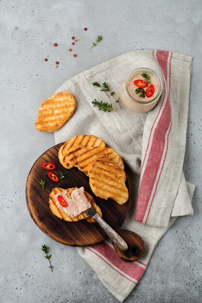 Pâté de poulet maison à partir de foie avec du poivron rouge, des brindilles de thym et des tranches de pain grillé sur une vieille planche en bois sur du béton gris ou de la pierre.