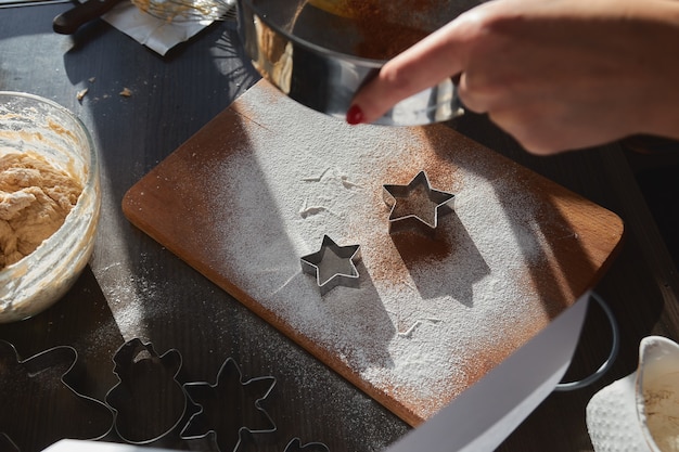 Pâte pour biscuits au pain d'épice roulée sur la planche de bois en découpant des biscuits en forme d'étoile