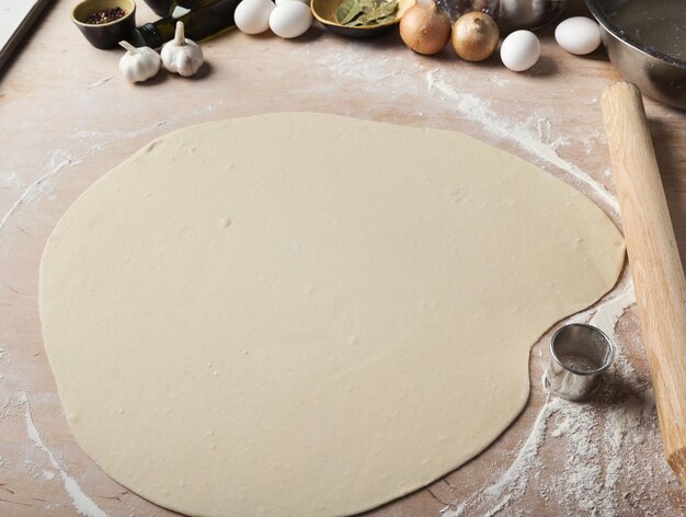 Pâte ronde roulée mince avec de la farine sur la table de la cuisine. Préparation de la couche de gâteau, vareniki ou boulettes