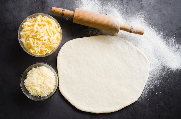 Pâte roulée, farine à cuire, fromage râpé et rouleau à pâtisserie sur un tableau noir.