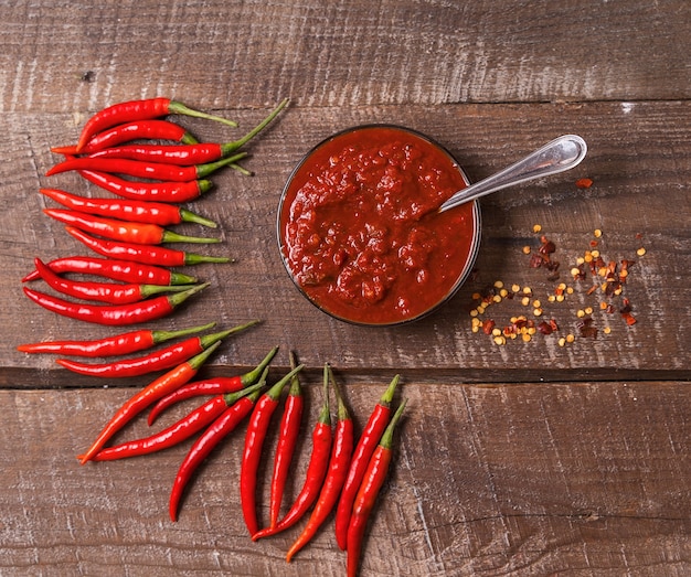 Pâte de sauce au piment fort harissa, traditionnelle tunisienne, marocaine, cuisine arabe adjika, épices de piment et piments rouges frais, sur table en bois.