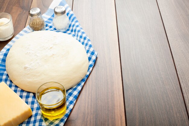 Pâte sur une table en bois, sur une serviette de cuisine bleue, avec de l'huile d'olive, du sel et du poivre et de la crème sure