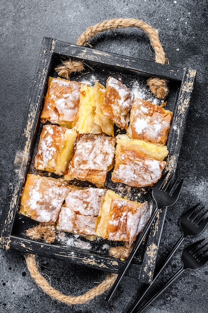 Pâte à tarte Bougatsa tranchée avec crème pâtissière à la semoule. Fond noir. Vue de dessus.